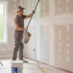 Un bricoleur prépare un mur pour la peinture avec des outils et matériaux autour.